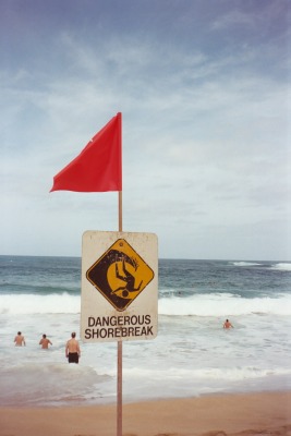 Waimea Bay sign: Dangerous shorebreak. Swimmers in the distance.